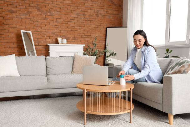 Young woman with laptop and air humidifier on table at home - Photo, Image