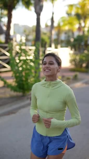 Žena běhá venku ve žlutých horních a modrých kraťasech a užívá si slunečného dne obklopeného zelení - Záběry, video