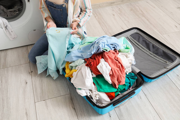 Kirli çamaşırları bavulunda bej arka planda çamaşır makinesinin yanında taşıyan genç bir kadın. - Fotoğraf, Görsel