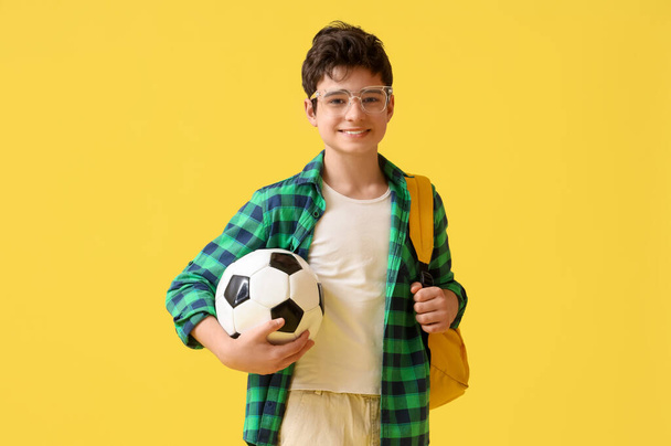 Підлітковий хлопчик з футбольним м'ячем на жовтому фоні - Фото, зображення