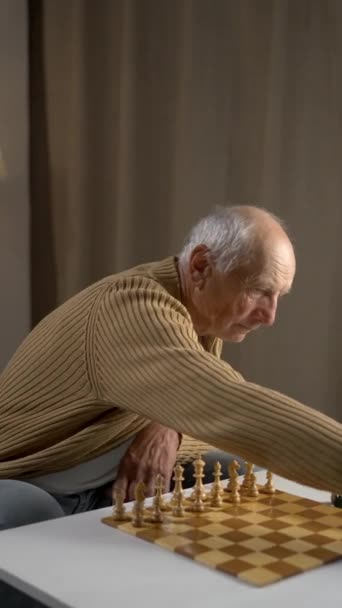Egy idős ember mélyen belemerül egy sakkjátszmába, és figyelmesen koncentrál, miközben egy kényelmes asztalnál ül. - Felvétel, videó