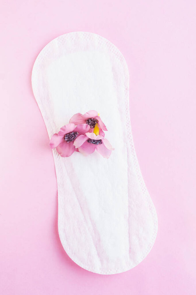 白いパントリーライナーに置かれた3つのピンクの花,月経血の比喩. ピンクのバックグラウンドで孤立。 女性衛生,衛生ナプキン,月経の概念. 垂直スタジオショット. - 写真・画像