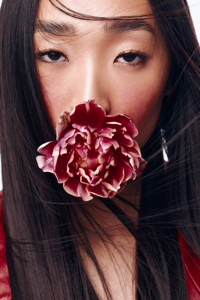 Piękna kobieta z długimi czarnymi włosami wydmuchująca kwiat z twarzy w delikatnym wietrze - Zdjęcie, obraz