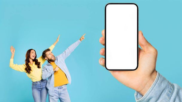 Remek ajánlat. Boldog fiatal pár táncol és mutat óriás mobiltelefon mutatja üres hely a modellezés design, kéz tartja fehér képernyő - Fotó, kép