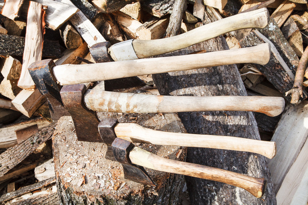 machados em bloco de madeira perto de pilha de lenha
 - Foto, Imagem