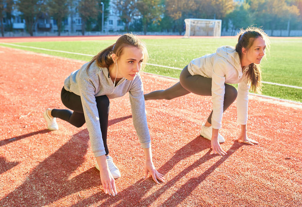 Дві дівчини в спортивному одязі готуються бігати на біговому стадіоні
 - Фото, зображення