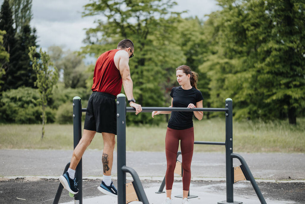 A man and a woman engage in a workout routine using bars at a park surrounded by green trees, focusing on fitness and health. - Valokuva, kuva