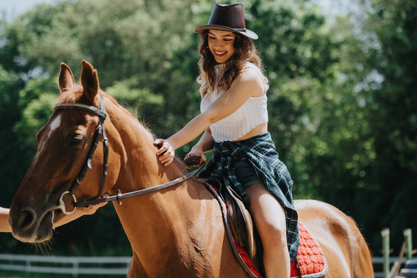 Onnellinen nuori nainen ratsastaa hevosella vehreyden ympäröimänä kauniina aurinkoisena päivänä. Ulkoseikkailu ja yhteys luontoon. - Valokuva, kuva
