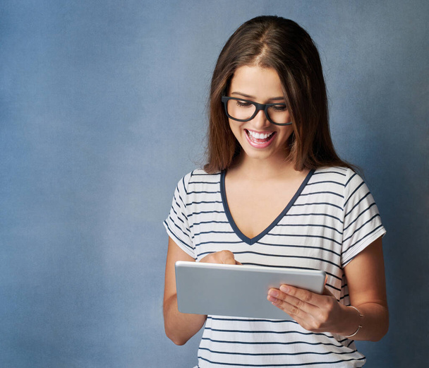 Щаслива жінка, окуляри і читання з планшетом для новин, онлайн-перегляд або дослідження на синьому фоні студії. Жінка, працівник або молодий дизайнер з посмішкою на технологіях для соціальних медіа. - Фото, зображення