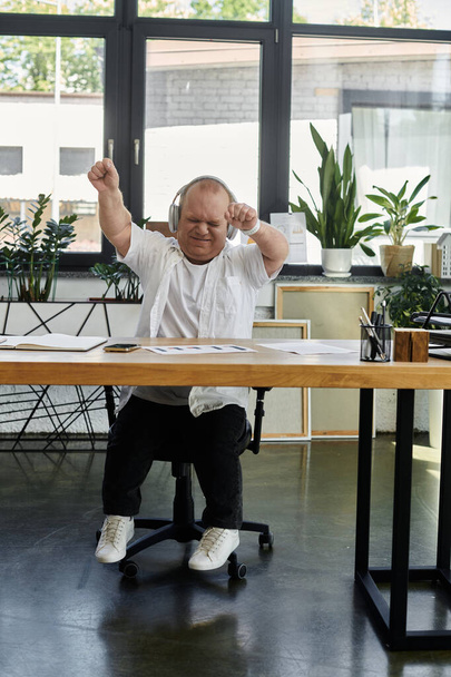 Ένας άνδρας με εγκλειστικότητα σε ένα γραφείο που χορεύει φορώντας ακουστικά, απολαμβάνοντας μια στιγμή διασκέδασης. - Φωτογραφία, εικόνα