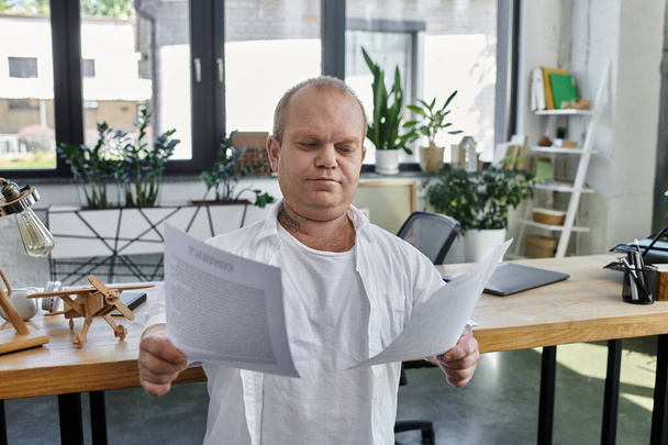 Чоловік з обмеженими можливостями у білій сорочці сидить за столом в офісі, ретельно розглядаючи документи. - Фото, зображення