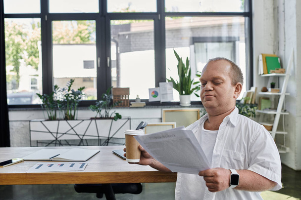 Egy inkluzivitású férfi felülvizsgálja a papírmunkát egy íróasztalnál egy modern irodai környezetben. - Fotó, kép