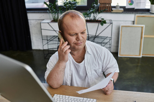 Un hombre con inclusividad en un entorno de oficina, trabajando diligentemente mientras está en una llamada telefónica. - Foto, Imagen