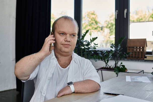 Un homme avec inclusivité est assis à son bureau, écoutant attentivement un appel téléphonique. - Photo, image