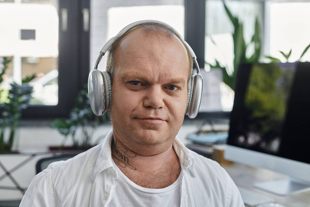 Muž s inkluzivitou ve sluchátkách pracuje u svého stolu v moderní kanceláři.. - Fotografie, Obrázek