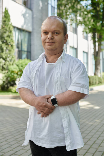 Un hombre con inclusividad vistiendo una camisa blanca se para en una calle de la ciudad. - Foto, imagen