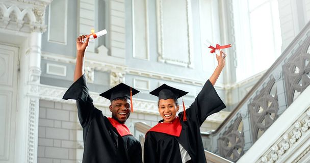 Zwei jubelnde Absolventen in Mützen und Kleidern feiern ihren erfolgreichen Abschluss und halten ihre Diplome in der Hand, die eine bedeutende akademische Leistung und eine strahlende Zukunft vor sich symbolisieren. - Foto, Bild