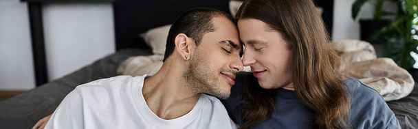 Una giovane coppia gay condivide un momento tenero nella loro camera da letto, le loro fronti si toccano mentre chiudono gli occhi. - Foto, immagini