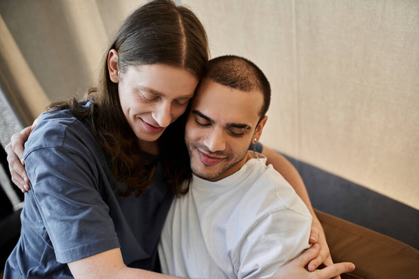 Um jovem casal gay compartilha um abraço amoroso dentro de uma casa moderna. - Foto, Imagem