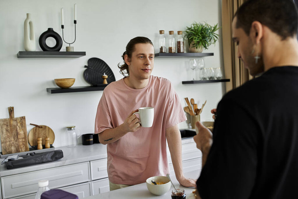 Молода гей-пару насолоджується ранком разом, обмінюючись кавою та розмовою на їхній сучасній кухні. - Фото, зображення