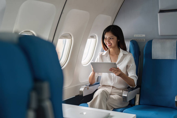 Profesjonalista biznesowy korzystający z tabletu w nowoczesnym samolocie, prezentujący wygodną i wydajną przestrzeń roboczą podczas podróży służbowych. - Zdjęcie, obraz