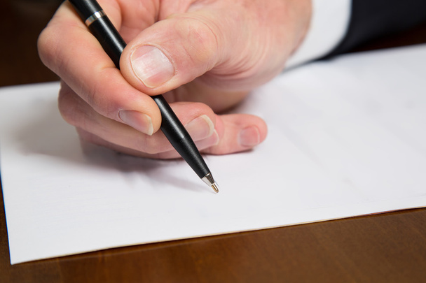 Hand of a businessman holding a pen over a paper - Fotoğraf, Görsel