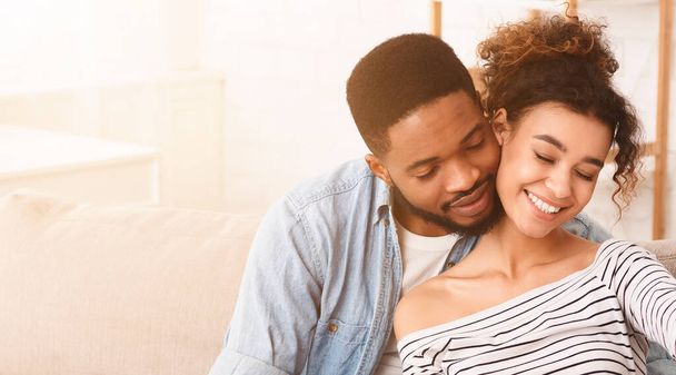 Homens e mulheres afro-americanos estão sentados juntos em um sofá em uma sala de estar. Eles aparecem relaxados e envolvidos em conversa, abraços, espaço de cópia - Foto, Imagem