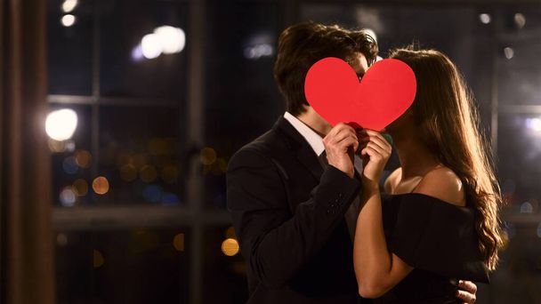 Linda pareja enamorada besándose detrás de un corazón de papel. Celebrando el concepto de San Valentín, espacio para copiar
. - Foto, imagen