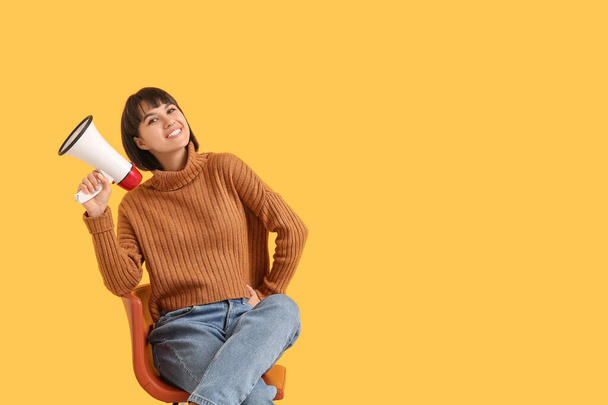 Mujer joven con megáfono sentado en la silla sobre fondo amarillo - Foto, imagen