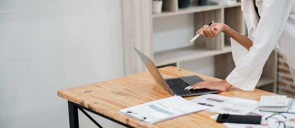 Geschäftsprofi arbeitet am Laptop am Schreibtisch mit Dokumenten und Diagrammen, analysiert Daten und hält einen Stift in der Hand. - Foto, Bild