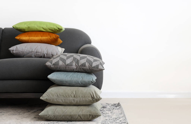 Sofá gris con pilas de almohadas cerca de la pared blanca - Foto, imagen