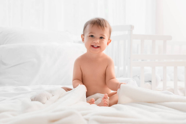 Little baby with towel sitting on bed after bathing in bedroom - Photo, Image