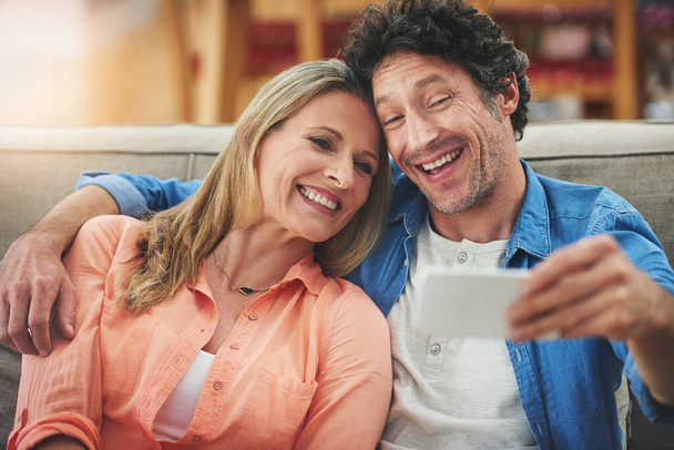 Para, selfie i sofa w domu, uśmiech i podekscytowany do pamięci z więzi z miłości z połączenia. Ludzie, mężczyzna i kobieta objęci opieką, szczęśliwe i profilowe zdjęcie w aplikacji na portalach społecznościowych. - Zdjęcie, obraz