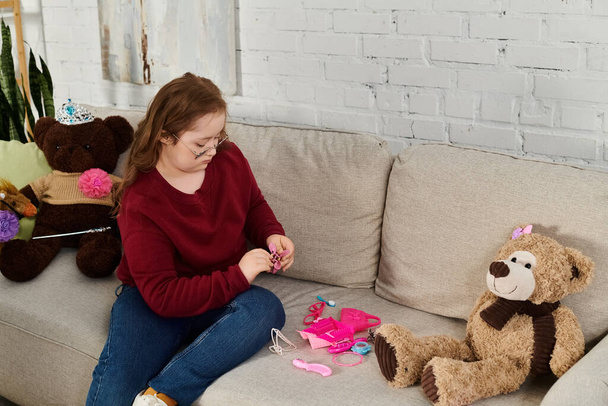 Uma menina com síndrome de Down brinca com seus brinquedos no sofá em casa. - Foto, Imagem