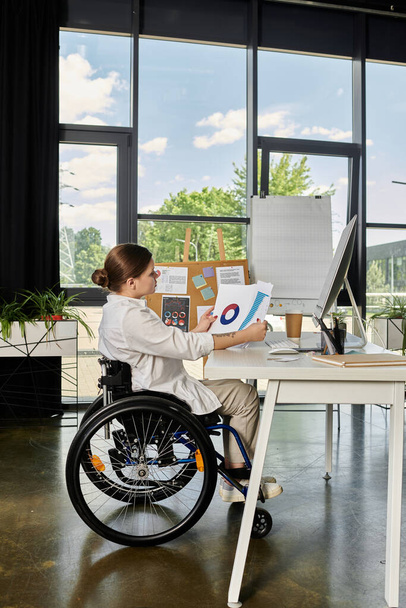 Μια νεαρή επιχειρηματίας σε αναπηρική καρέκλα εργάζεται στο γραφείο της σε ένα σύγχρονο γραφείο. - Φωτογραφία, εικόνα