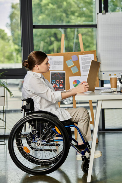 Eine junge Geschäftsfrau im Rollstuhl arbeitet an ihrem Schreibtisch in einem modernen Büro. - Foto, Bild