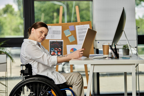 Μια νεαρή επιχειρηματίας σε αναπηρικό καροτσάκι εργάζεται στο γραφείο της σε ένα σύγχρονο γραφείο, επιδεικνύοντας την ένταξή της στον χώρο εργασίας. - Φωτογραφία, εικόνα