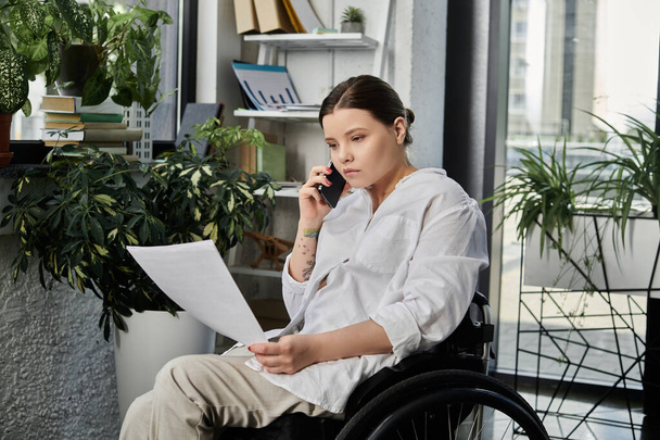 Une jeune femme d'affaires en fauteuil roulant travaille dans un bureau moderne, faisant preuve d'inclusion sur le lieu de travail. - Photo, image