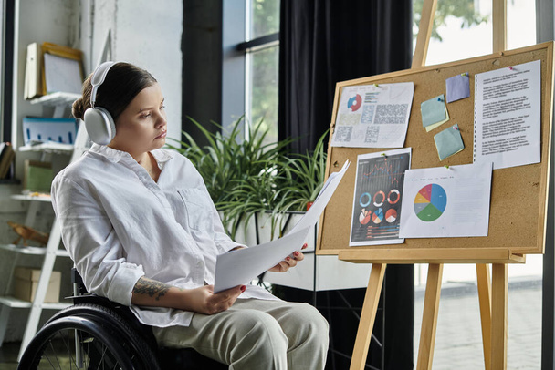 Una giovane donna d'affari con disabilità si siede sulla sedia a rotelle, esaminando i documenti in un ambiente ufficio moderno. - Foto, immagini