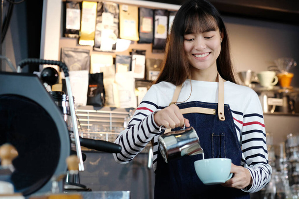 Jeunes femmes asiatiques barista verser du lait dans une tasse de café au comptoir du café, faire du café, latte art, concept de nourriture et de boisson - Photo, image