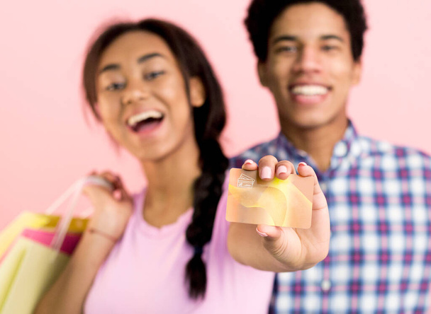 Spotřebitelský koncept. Teen pár s nákupními taškami, ukazuje kreditní kartu přes růžové pozadí - Fotografie, Obrázek