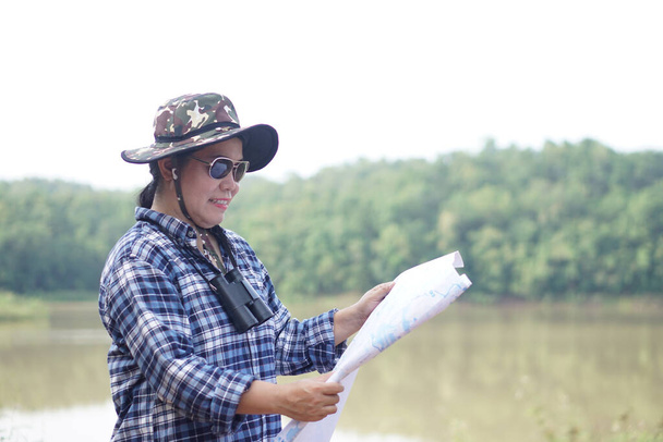 Mujer asiática exploradora sostiene mapa de papel para explorar la naturaleza en el bosque y la zona del lago. Concepto, exploración de la naturaleza. Estudio de ecología. Actividad pasatiempo, estilo de vida. Explorar el entorno          - Foto, Imagen