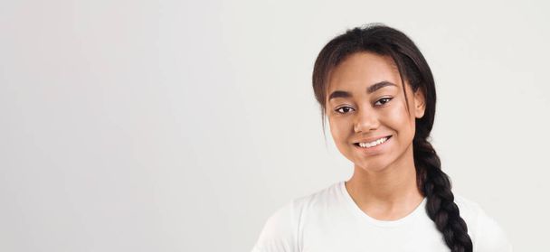 Chica joven afroamericana con el pelo trenzado está sonriendo brillantemente delante de un fondo blanco. Ella exuda alegría y felicidad mientras mira directamente a la cámara, panorama con espacio para copiar - Foto, Imagen
