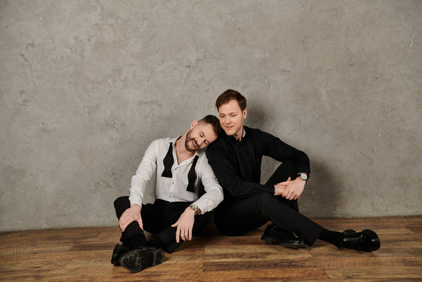 エレガントなスーツの2人の男性は,互いに傾いている柔らかい瞬間を共有します. - 写真・画像