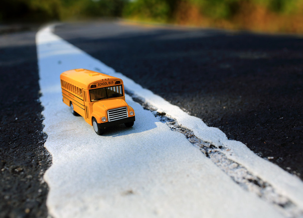 Modelo amarillo del juguete del autobús escolar en la carretera del país
 - Foto, imagen
