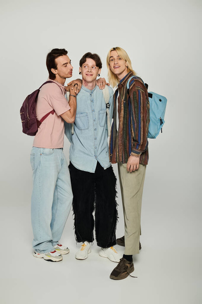 LGBTQIA topluluğunun üyeleri olan üç genç, gri bir arka plana karşı günlük giysiler içinde birlikte dururlar.. - Fotoğraf, Görsel