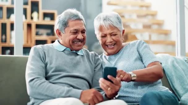 Senior couple, happy and phone on sofa with reading for funny memory with love, care and bonding with app. Old man, elderly woman and smile with smartphone, scroll or remember with comic chat in home. - Footage, Video