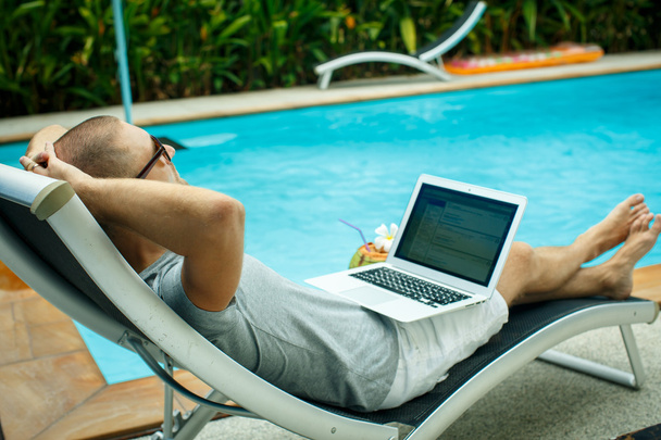A man with a laptop by the pool - Фото, изображение