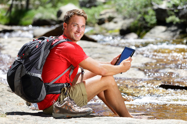 Man hiker relaxing by river holding ebook - Foto, Imagen