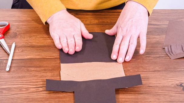 Stap voor stap. Leraar begeleidt online klas door het maken van een papieren pop uit een bruine tas, creatief met behulp van een houten oppervlak als werkruimte. - Foto, afbeelding